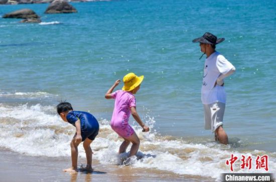 6月8日，海南三亚，游客在沙滩玩耍嬉戏。当日，恰逢世界海洋日，海南省三亚市天涯海角游览区迎来大批游客。蔚蓝海面游船穿梭，沙滩上游客尽情玩耍、拍摄留念，尽情感受海洋生态的独特魅力。中新社记者